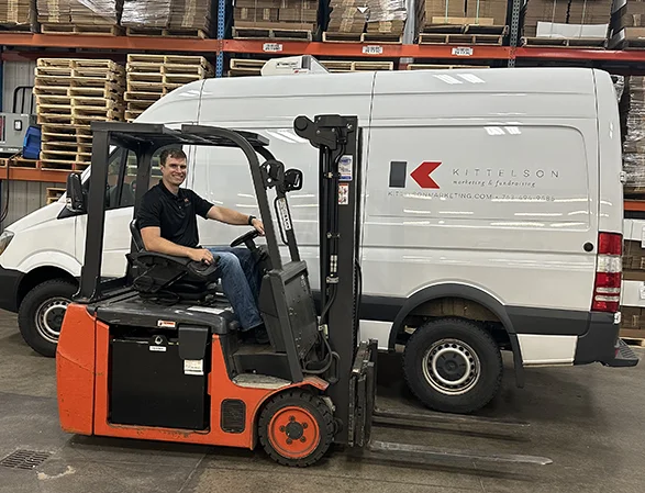 Kittelson Marketing team member operating forklift in warehouse with delivery van